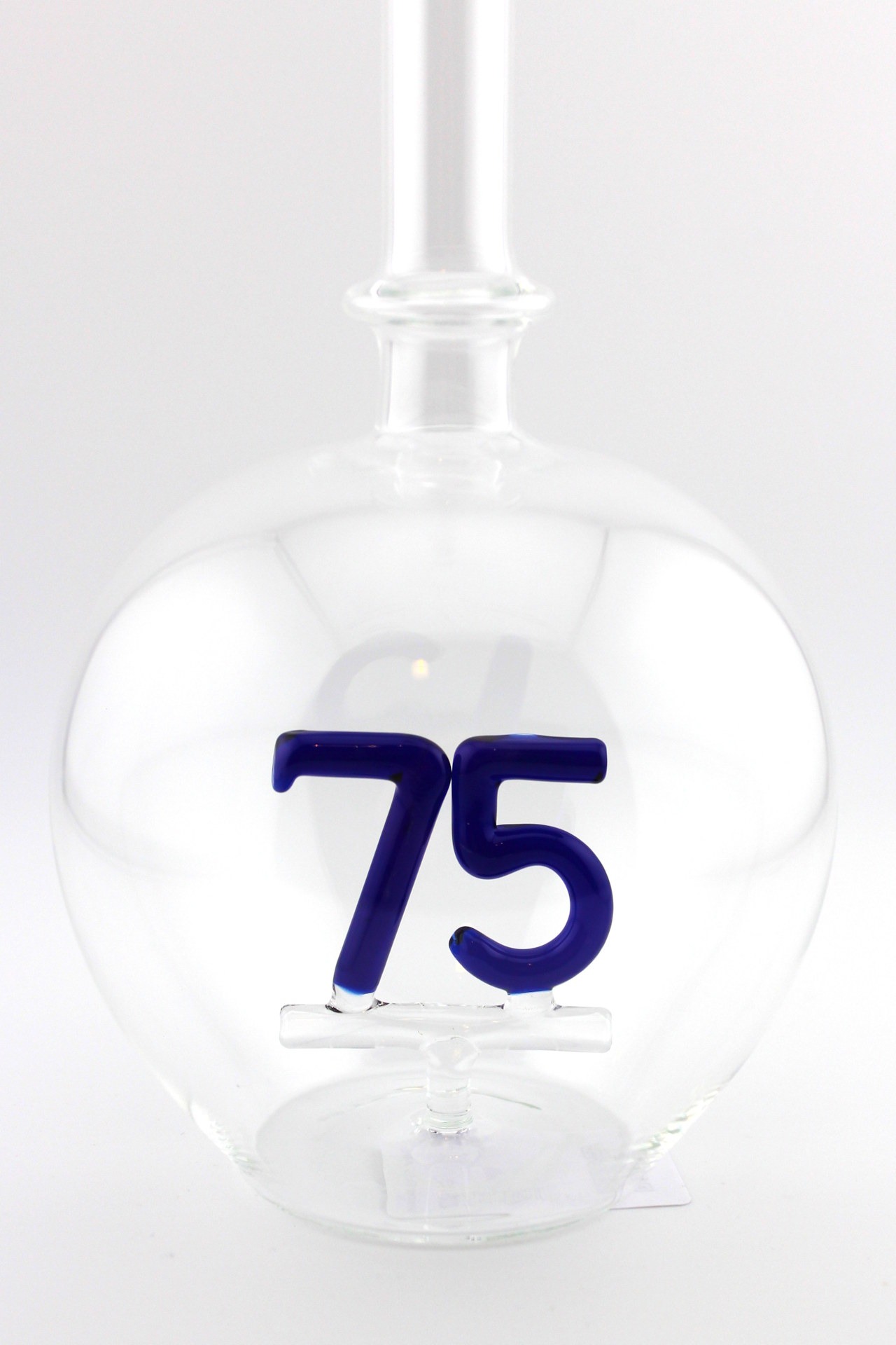 Eine leere bauchige Flasche aus Glas mit einer aus Glas geblasenen Zahl 75 im Inneren.