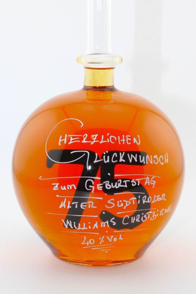 Eine mit Williams Christbirne befüllte bauchige Flasche aus Glas mit einer aus Glas geblasenen Zahl 75 im Inneren.