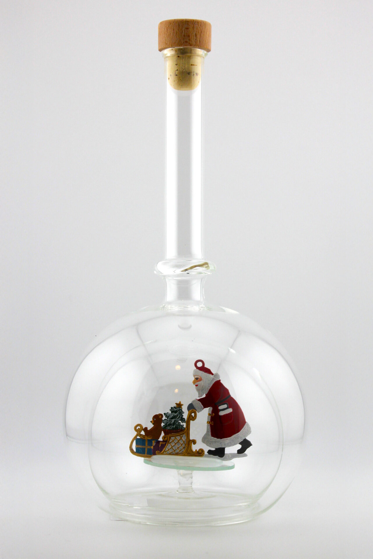 Eine leere bauchige Flasche aus Glas mit einem Schlitten schiebenden Weihnachtsmann im Inneren.