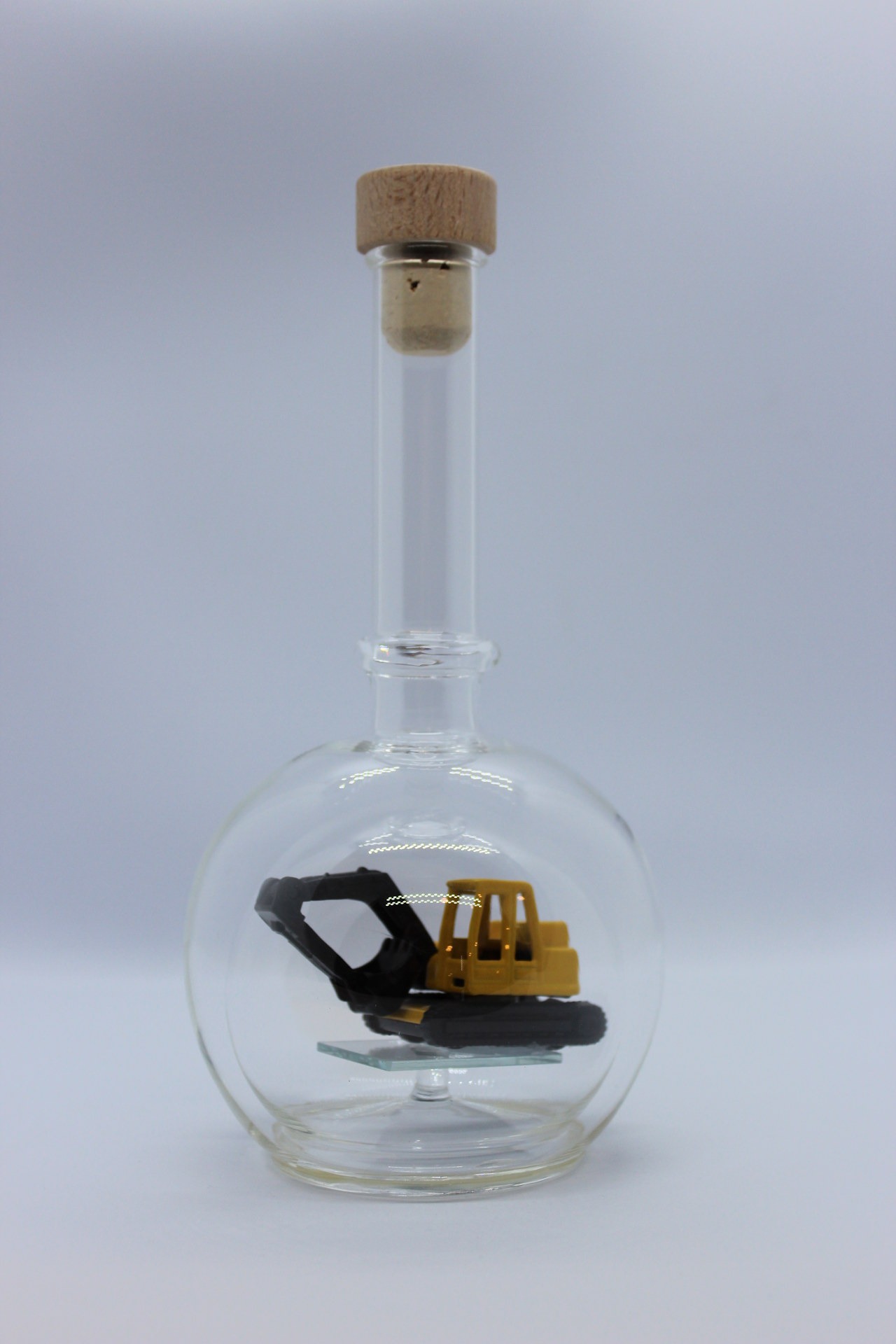 Eine leere bauchige Flasche aus Glas mit einem Bagger im Inneren.