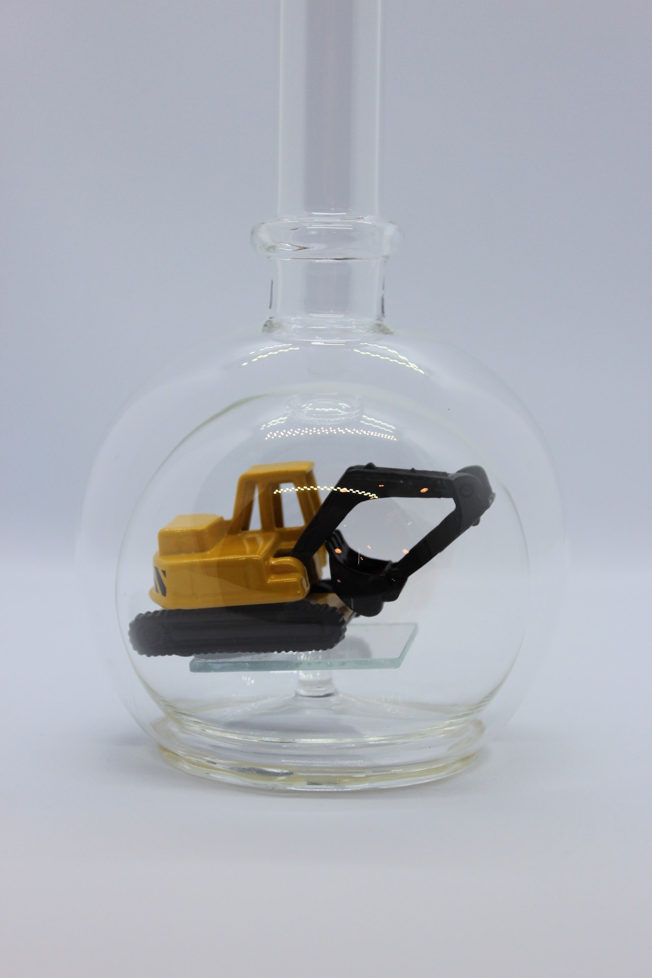 Eine leere bauchige Flasche aus Glas mit einem Bagger im Inneren.