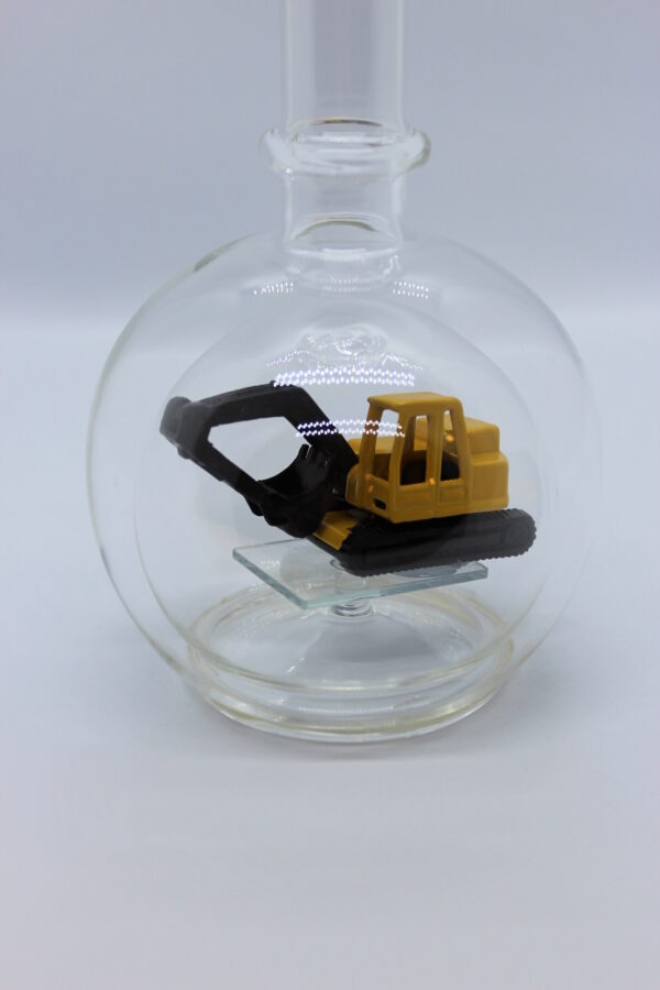 Eine leere bauchige Flasche aus Glas mit einem Bagger im Inneren.