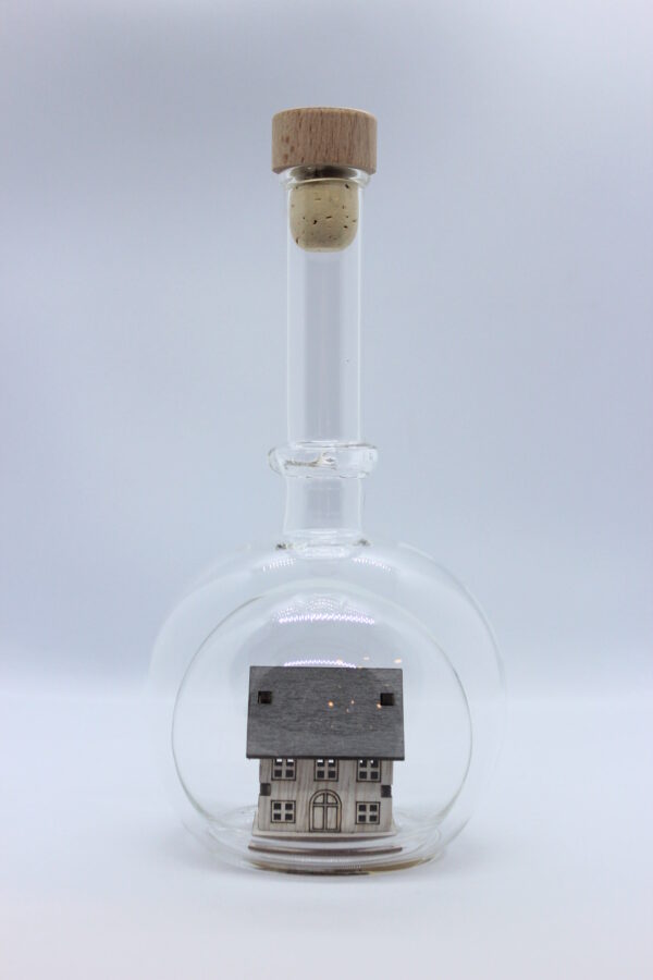 Eine leere bauchige Flasche aus Glas mit einem Haus / Eigenheim im Inneren.