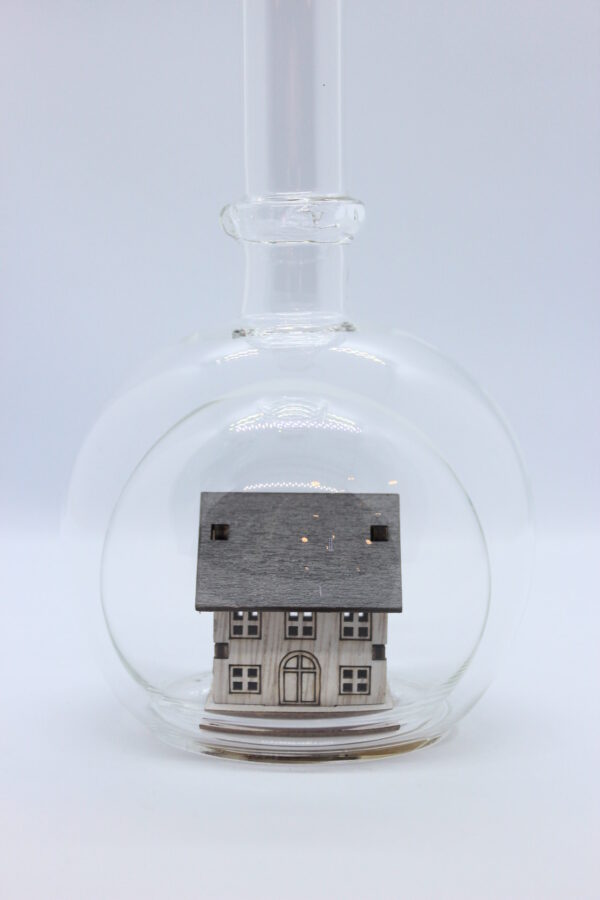 Eine leere bauchige Flasche aus Glas mit einem Haus / Eigenheim im Inneren.