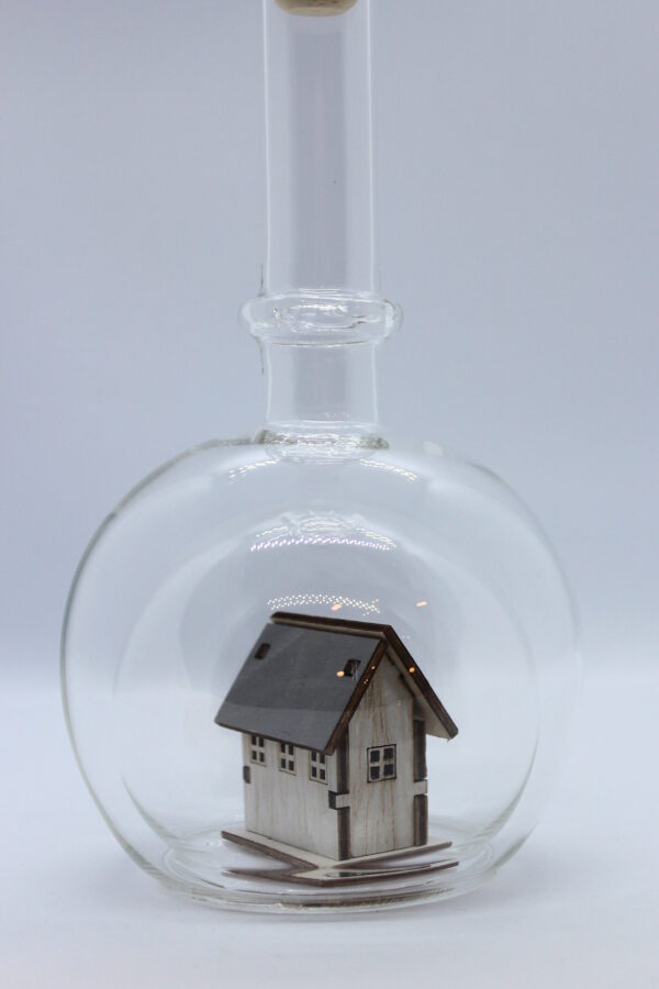 Eine leere bauchige Flasche aus Glas mit einem Haus / Eigenheim im Inneren.