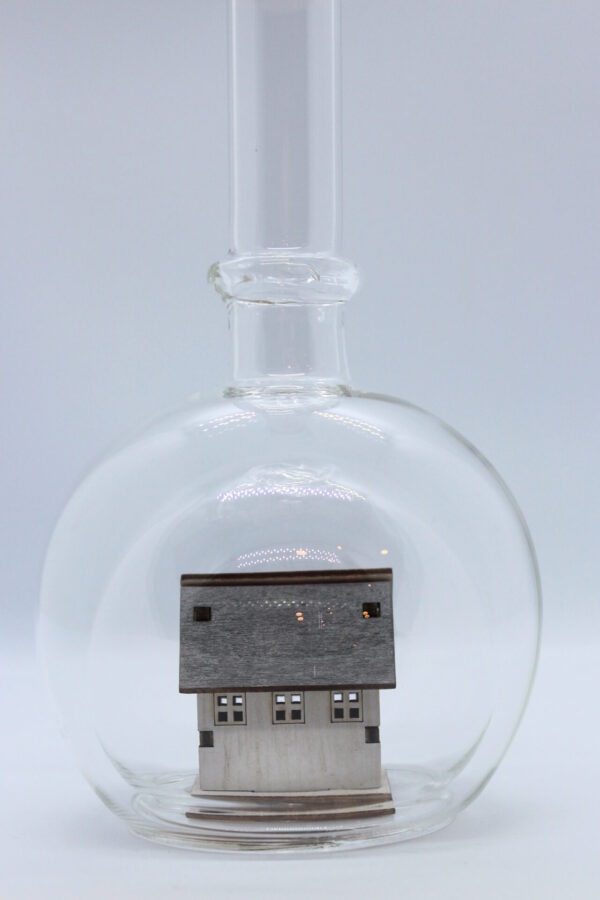 Eine leere bauchige Flasche aus Glas mit einem Haus / Eigenheim im Inneren.