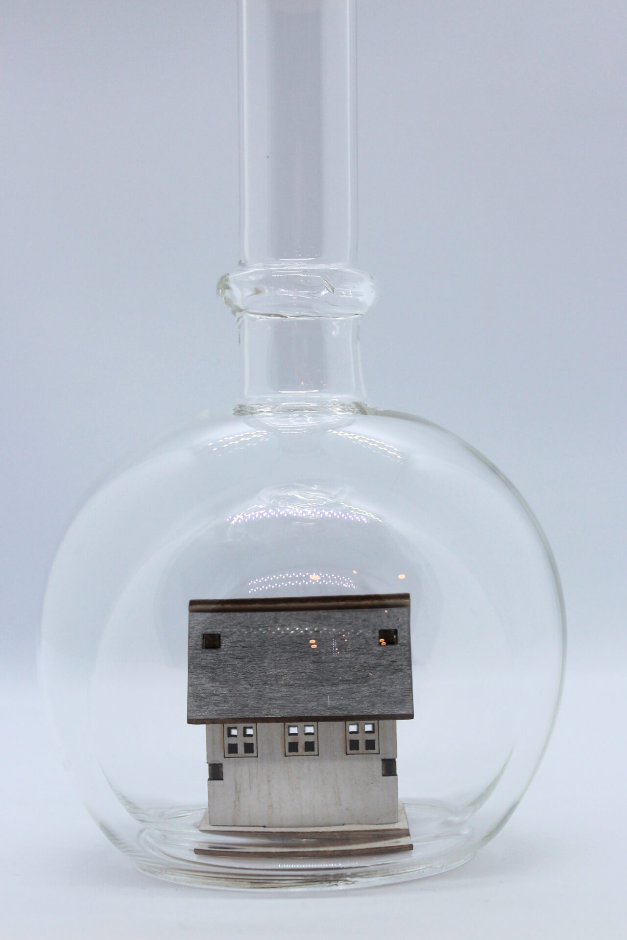Eine leere bauchige Flasche aus Glas mit einem Haus / Eigenheim im Inneren.
