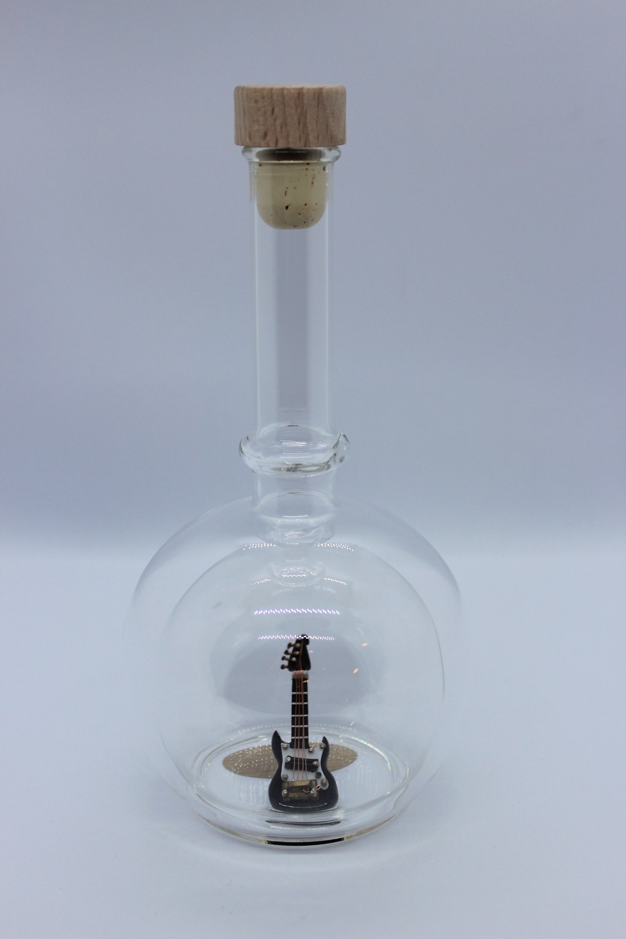 Eine leere bauchige Flasche aus Glas mit einer E-Gitarre im Inneren.