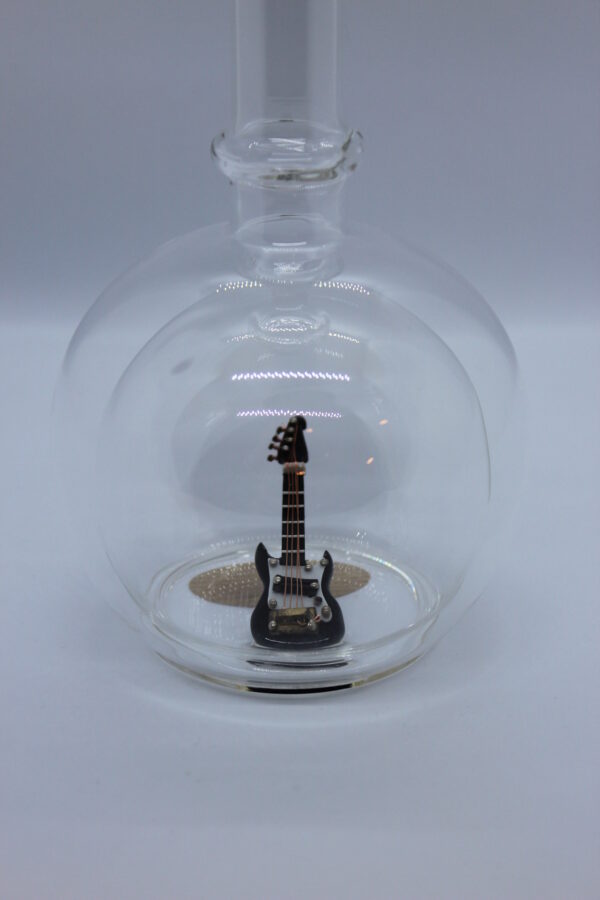 Eine leere bauchige Flasche aus Glas mit einer E-Gitarre im Inneren.