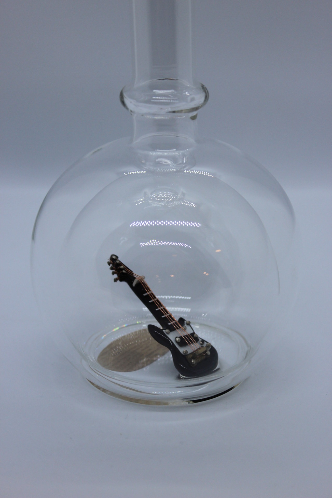 Eine leere bauchige Flasche aus Glas mit einer E-Gitarre im Inneren.