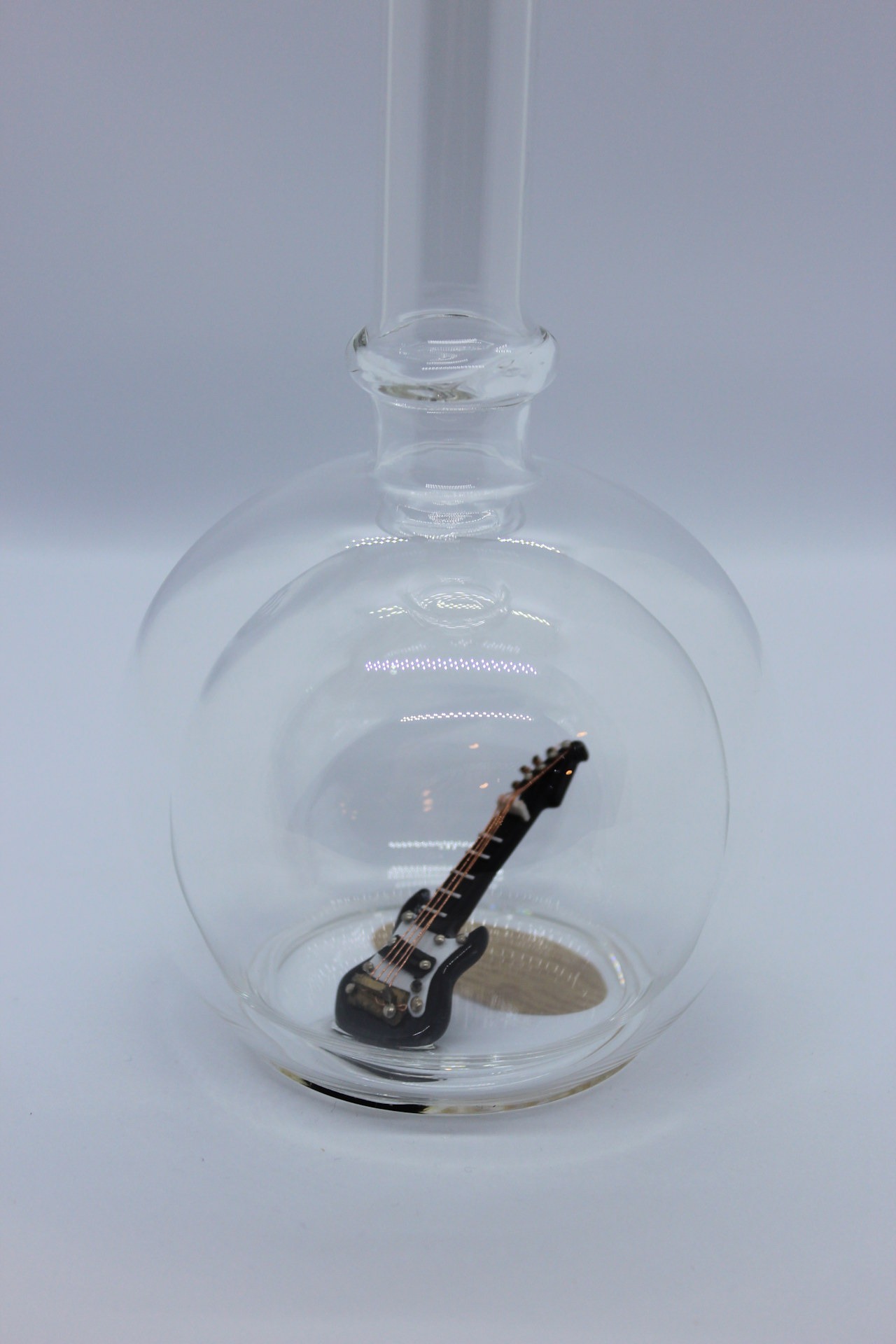 Eine leere bauchige Flasche aus Glas mit einer E-Gitarre im Inneren.