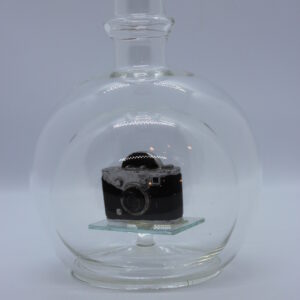 Magicflasche mit Fotoapparat 200 ml Eine leere bauchige Flasche aus Glas mit einem Fotoapparat im Inneren.