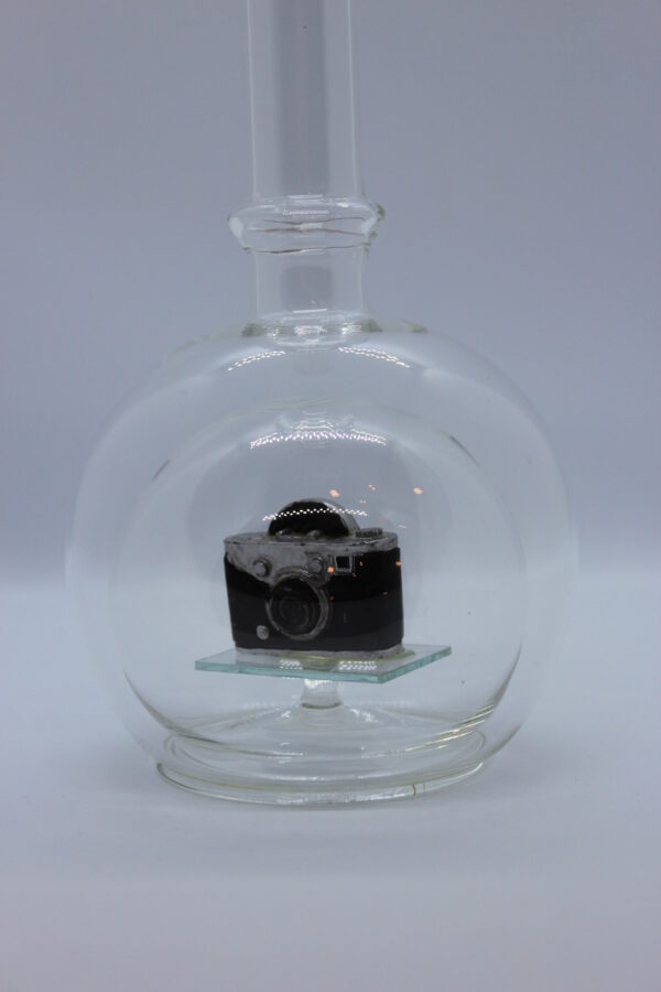 Eine leere bauchige Flasche aus Glas mit einem Fotoapparat im Inneren.