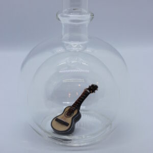 Eine leere bauchige Flasche aus Glas mit einer Gitarre im Inneren.