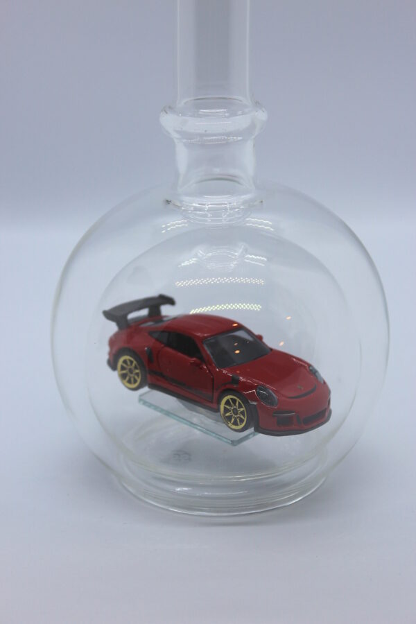Eine leere bauchige Flasche aus Glas mit einem roten Porsche im Inneren.