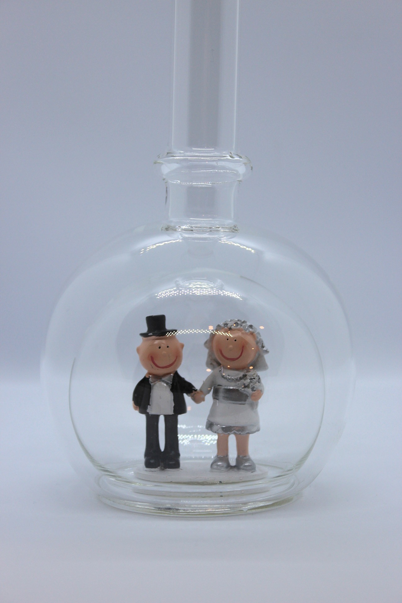 Eine leere bauchige Flasche aus Glas mit silbernem Hochzeitspaar im Inneren.