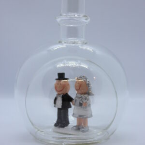 Eine leere bauchige Flasche aus Glas mit silbernem Hochzeitspaar im Inneren.