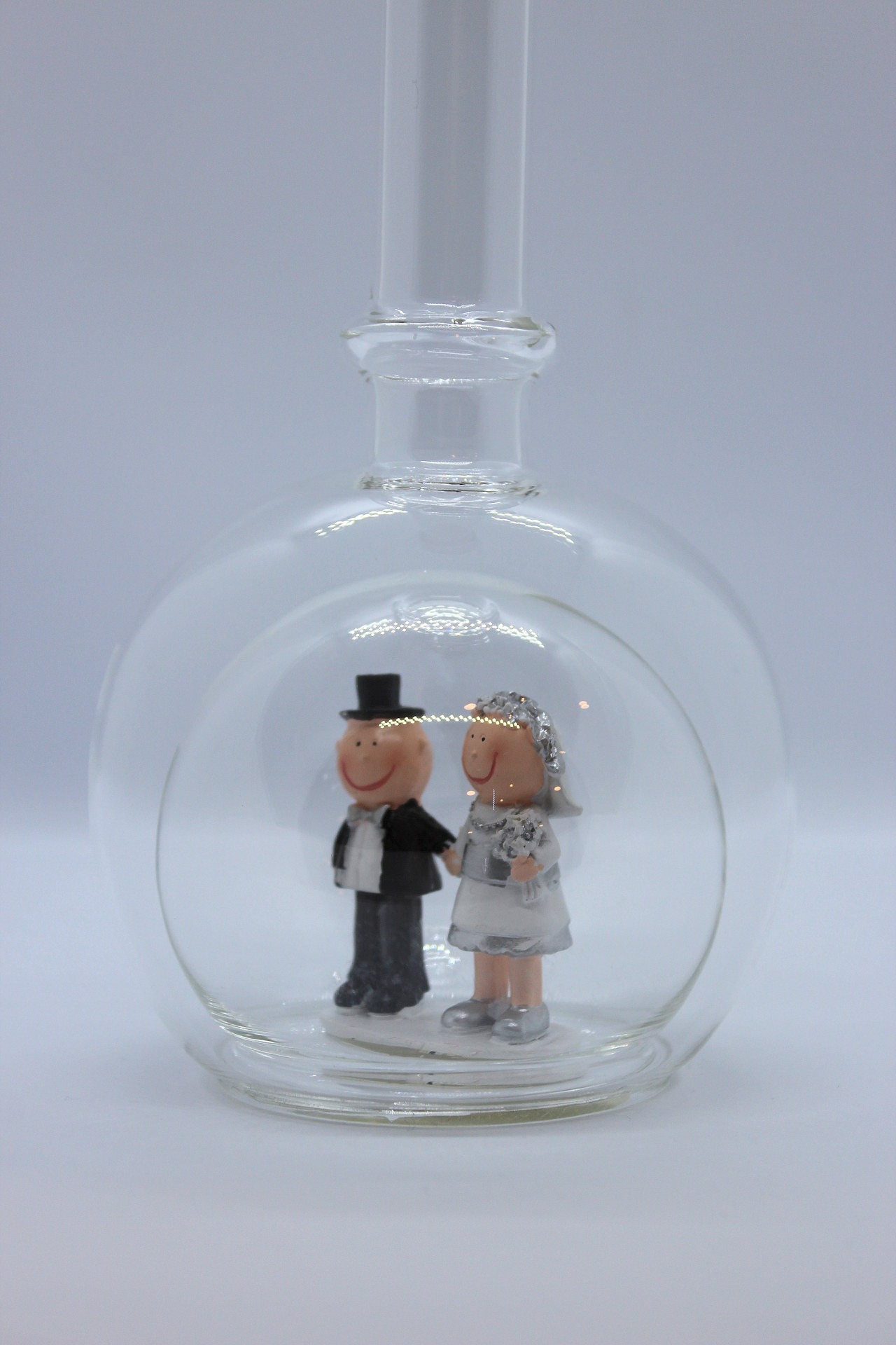 Eine leere bauchige Flasche aus Glas mit silbernem Hochzeitspaar im Inneren.