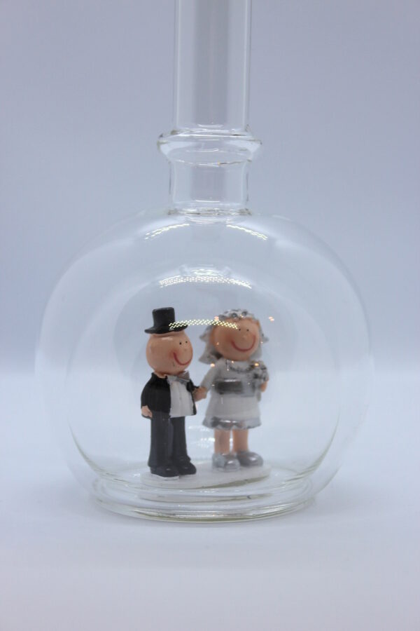 Eine leere bauchige Flasche aus Glas mit silbernem Hochzeitspaar im Inneren.