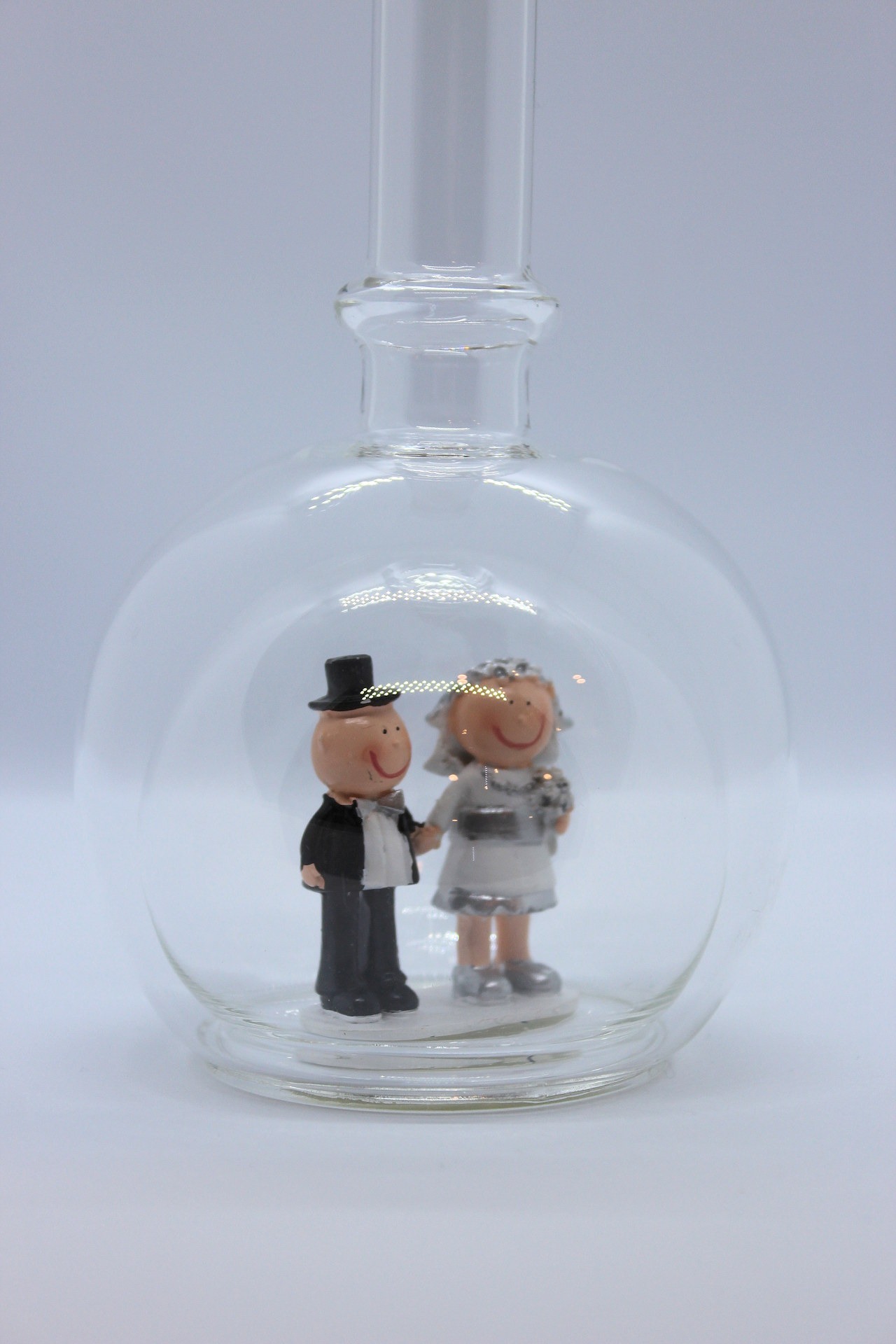 Eine leere bauchige Flasche aus Glas mit silbernem Hochzeitspaar im Inneren.