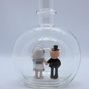 Eine leere bauchige Flasche aus Glas mit silbernem Hochzeitspaar im Inneren.