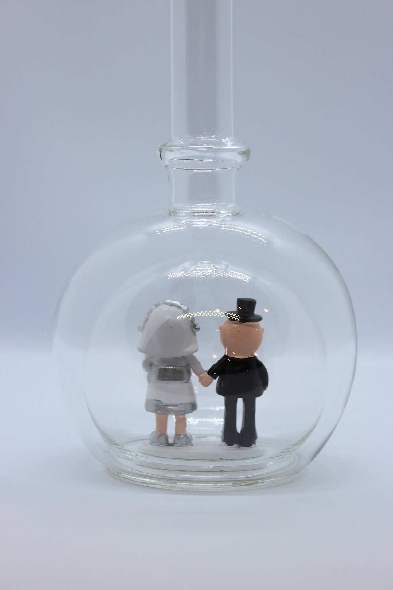 Eine leere bauchige Flasche aus Glas mit silbernem Hochzeitspaar im Inneren.