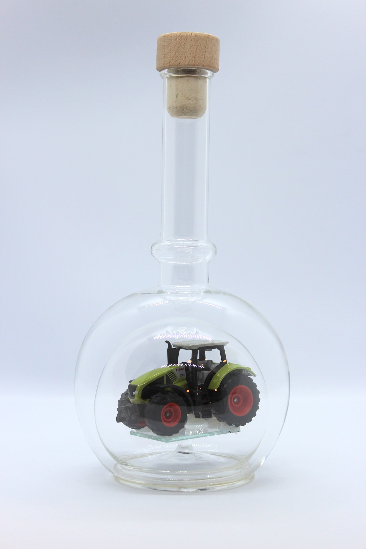 Eine leere bauchige Flasche aus Glas mit einem Claas-Traktor im Inneren.