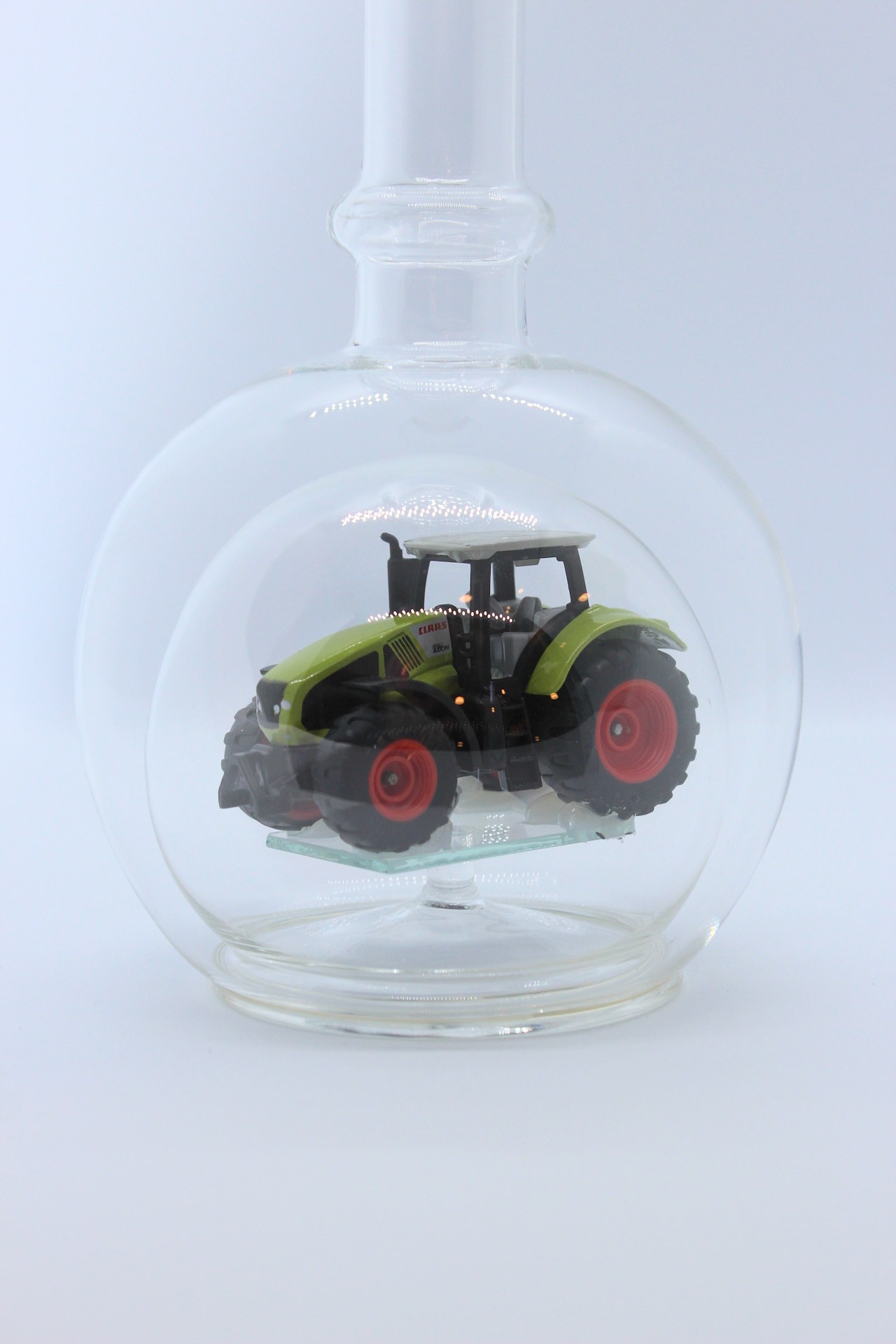 Eine leere bauchige Flasche aus Glas mit einem Claas-Traktor im Inneren.