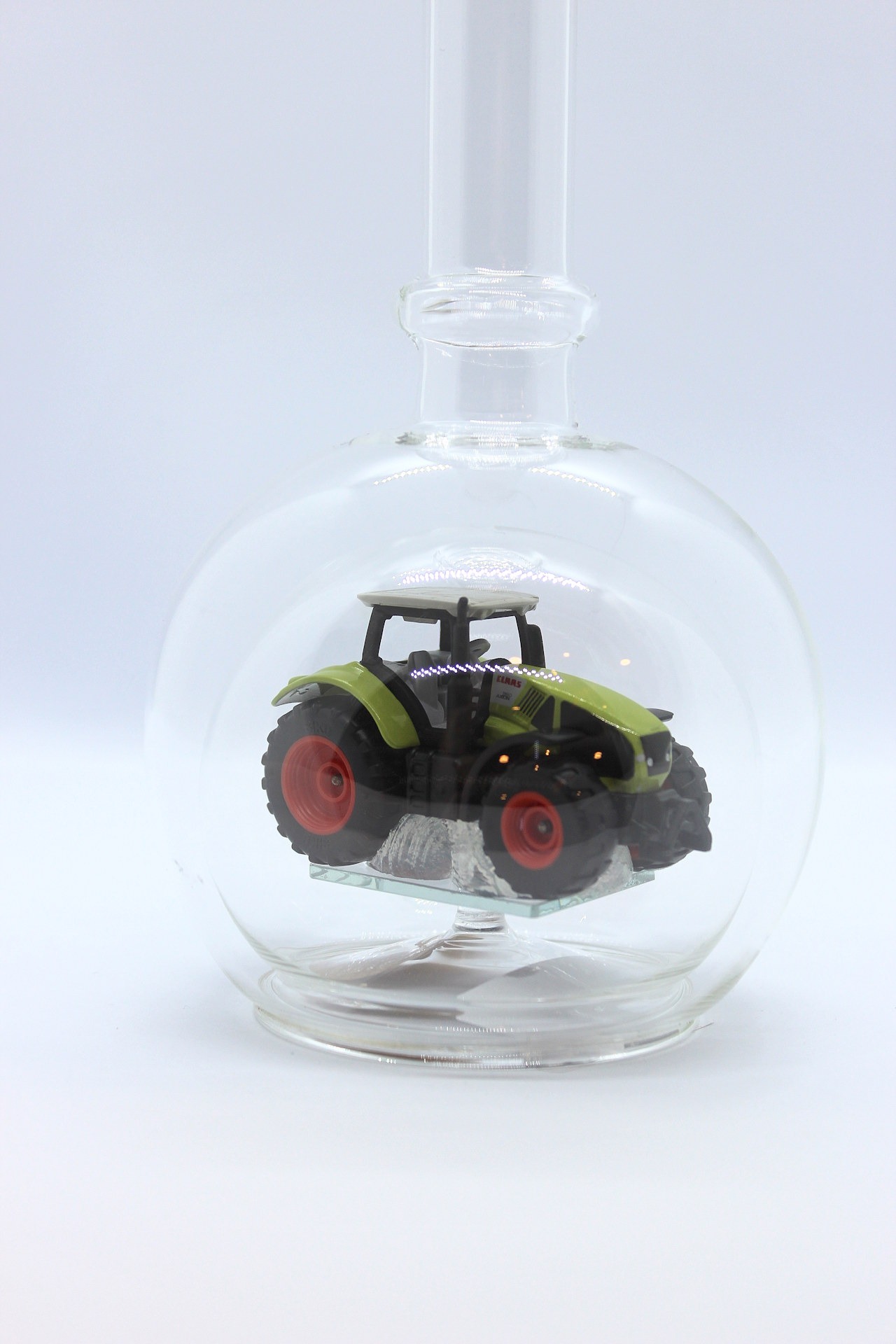 Eine leere bauchige Flasche aus Glas mit einem Claas-Traktor im Inneren.
