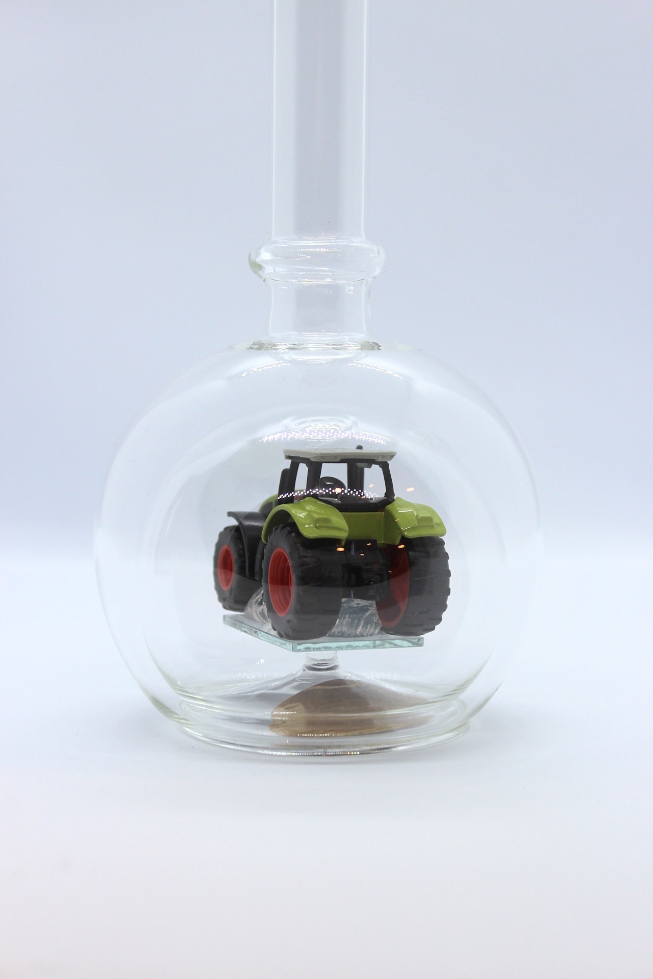 Eine leere bauchige Flasche aus Glas mit einem Claas-Traktor im Inneren.