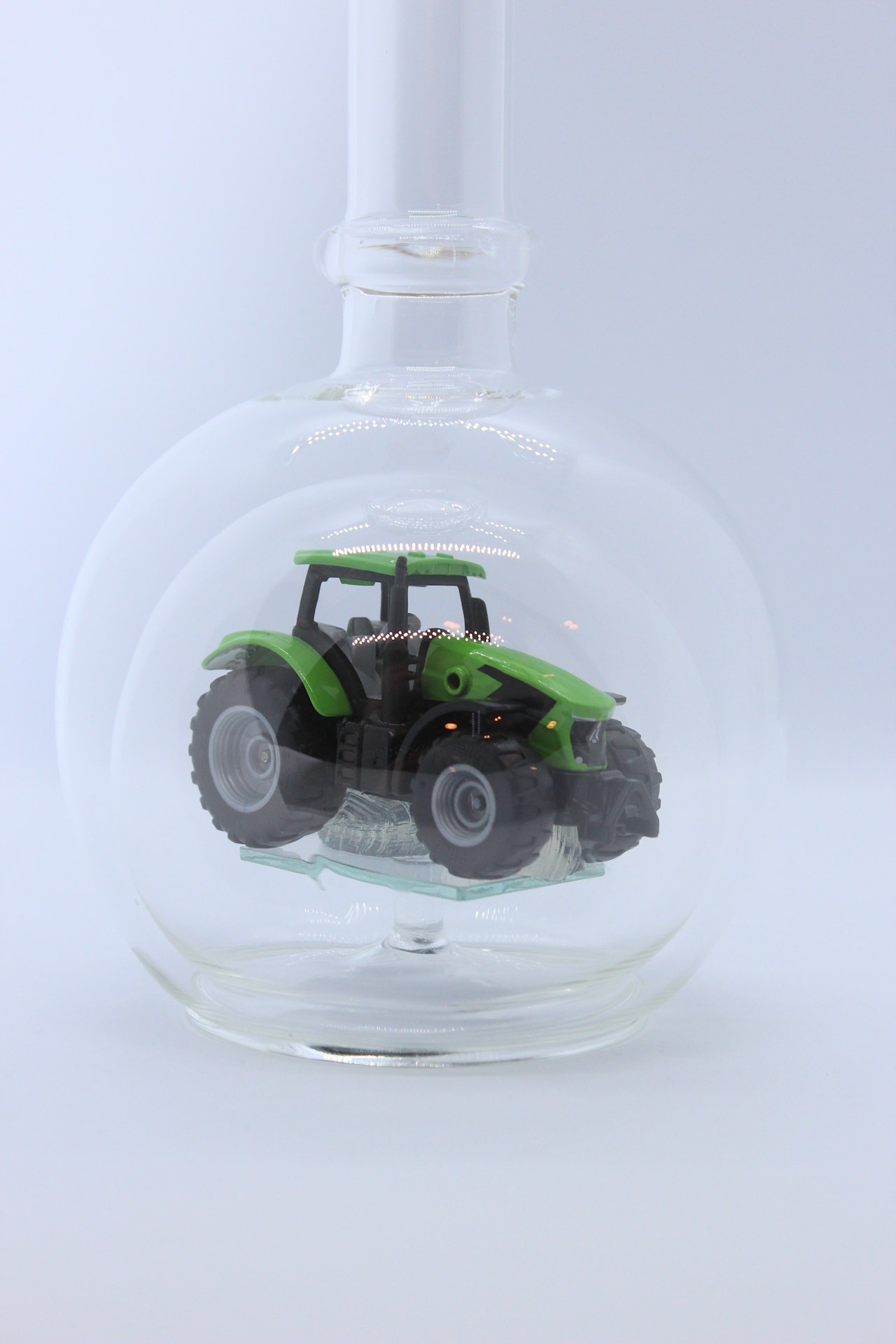 Eine leere bauchige Flasche aus Glas mit einem Deutz-Traktor im Inneren.