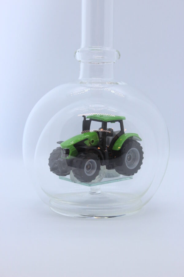 Eine leere bauchige Flasche aus Glas mit einem Deutz-Traktor im Inneren.