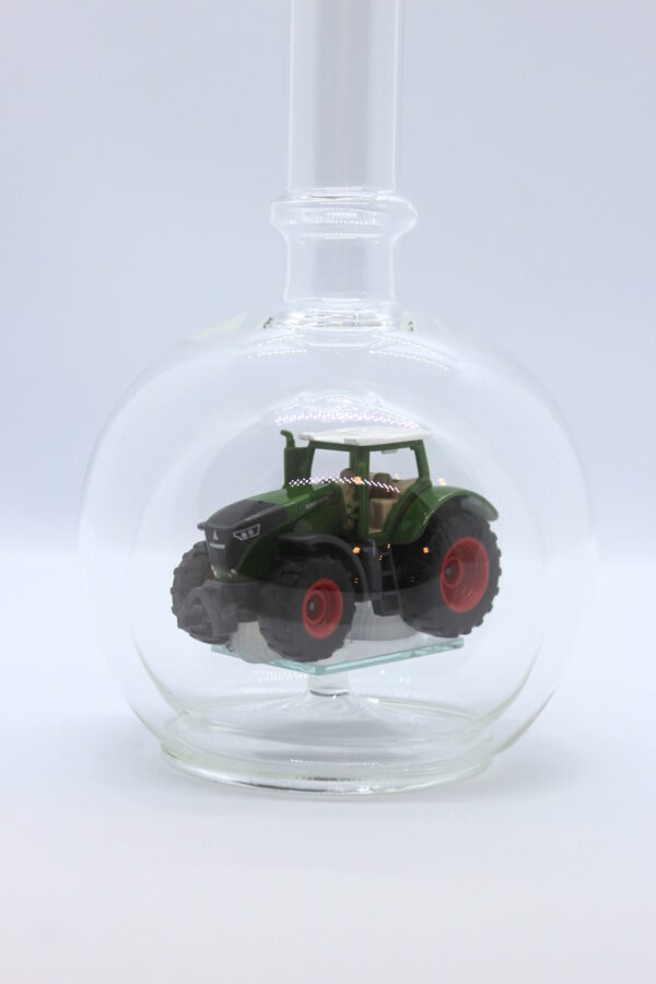 Eine leere bauchige Flasche aus Glas mit einem Fendt-Traktor im Inneren.