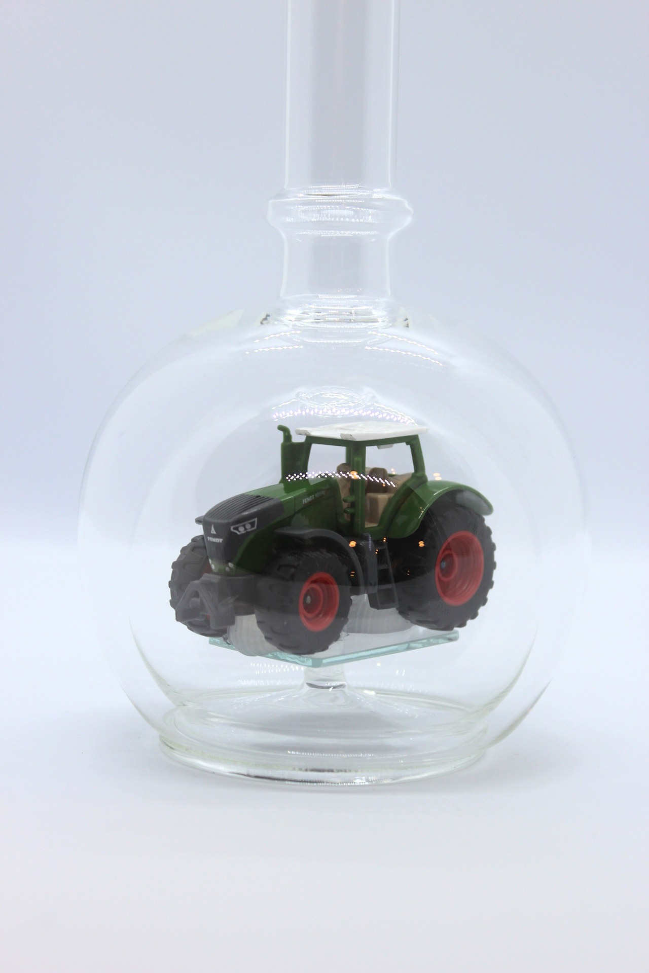 Eine leere bauchige Flasche aus Glas mit einem Fendt-Traktor im Inneren.