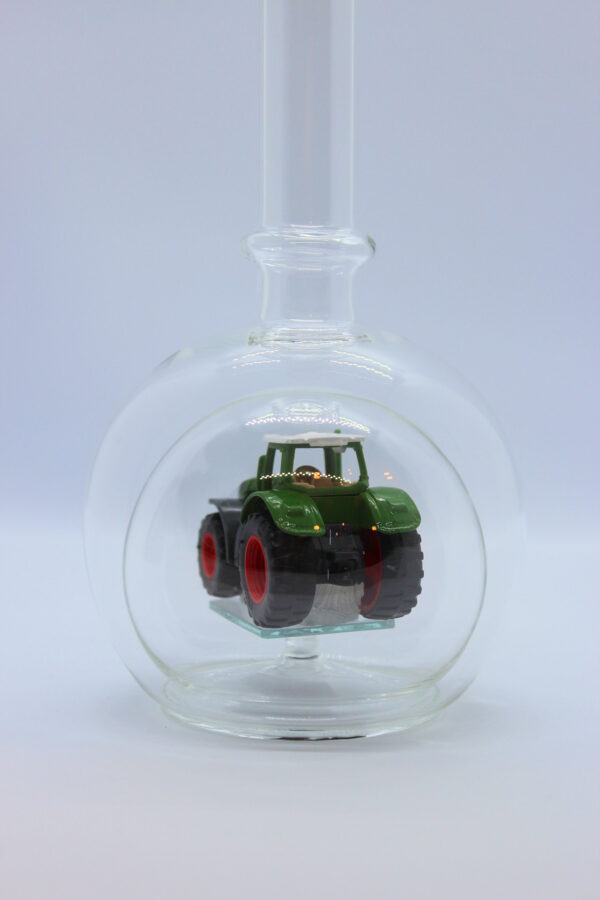 Eine leere bauchige Flasche aus Glas mit einem Fendt-Traktor im Inneren.