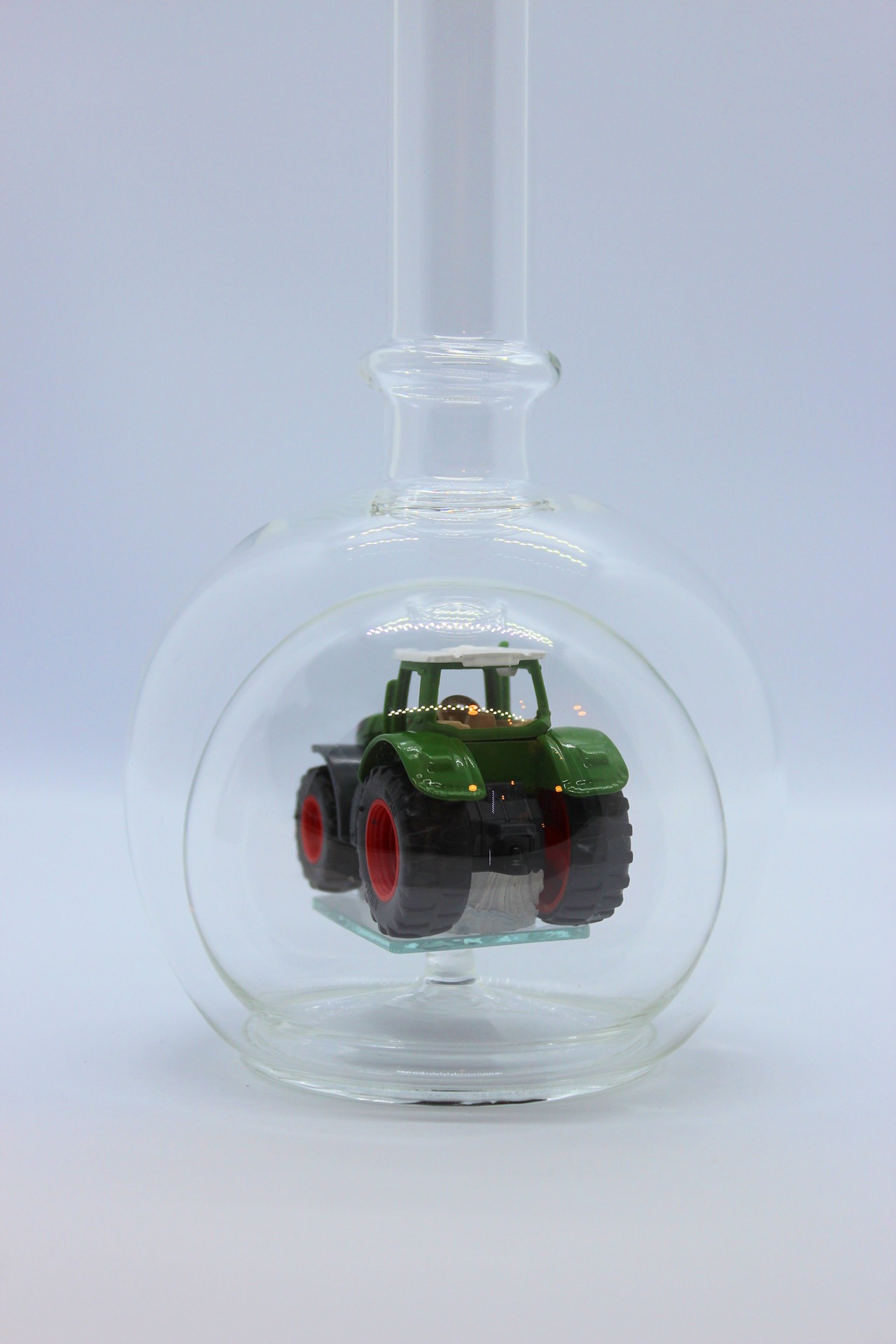 Eine leere bauchige Flasche aus Glas mit einem Fendt-Traktor im Inneren.