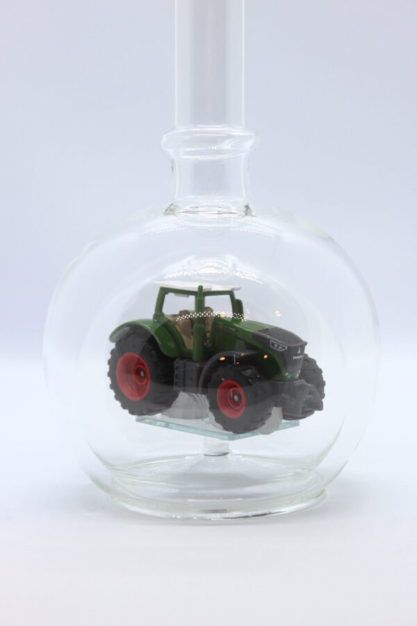 Eine leere bauchige Flasche aus Glas mit einem Fendt-Traktor im Inneren.