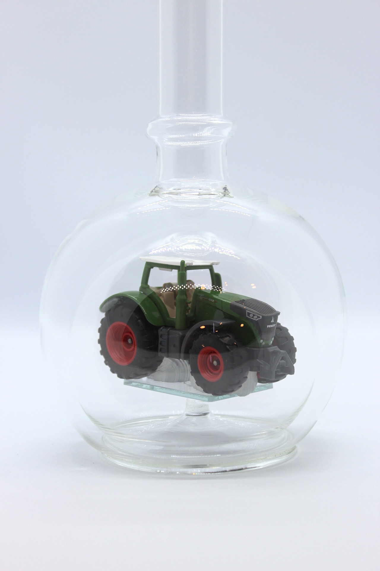 Eine leere bauchige Flasche aus Glas mit einem Fendt-Traktor im Inneren.
