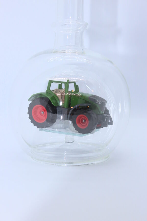 Eine leere bauchige Flasche aus Glas mit einem Fendt-Traktor im Inneren.