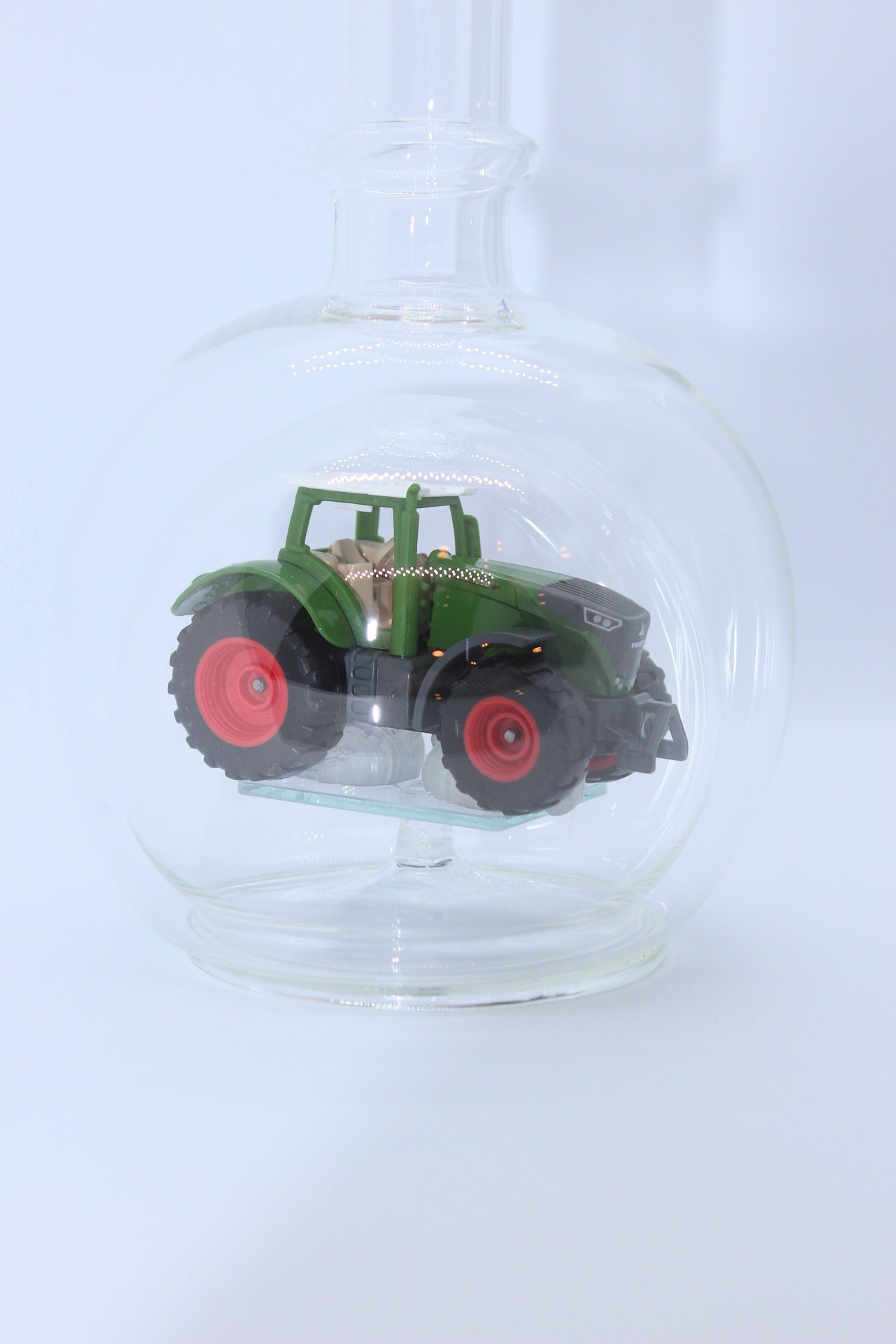 Eine leere bauchige Flasche aus Glas mit einem Fendt-Traktor im Inneren.