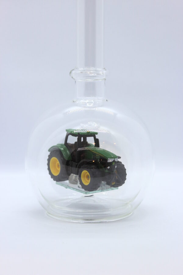 Eine leere bauchige Flasche aus Glas mit einem John-Deere-Traktor im Inneren.