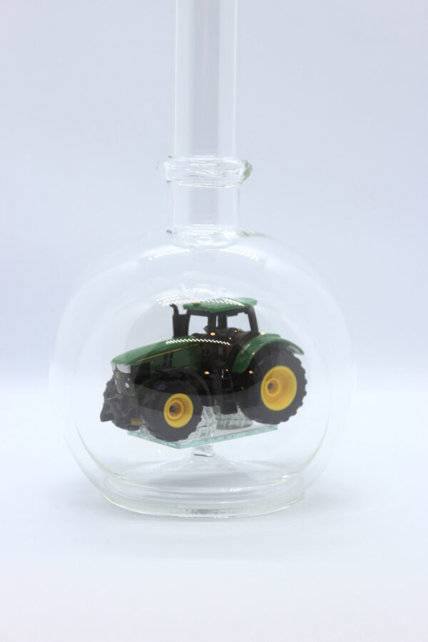 Eine leere bauchige Flasche aus Glas mit einem John-Deere-Traktor im Inneren.