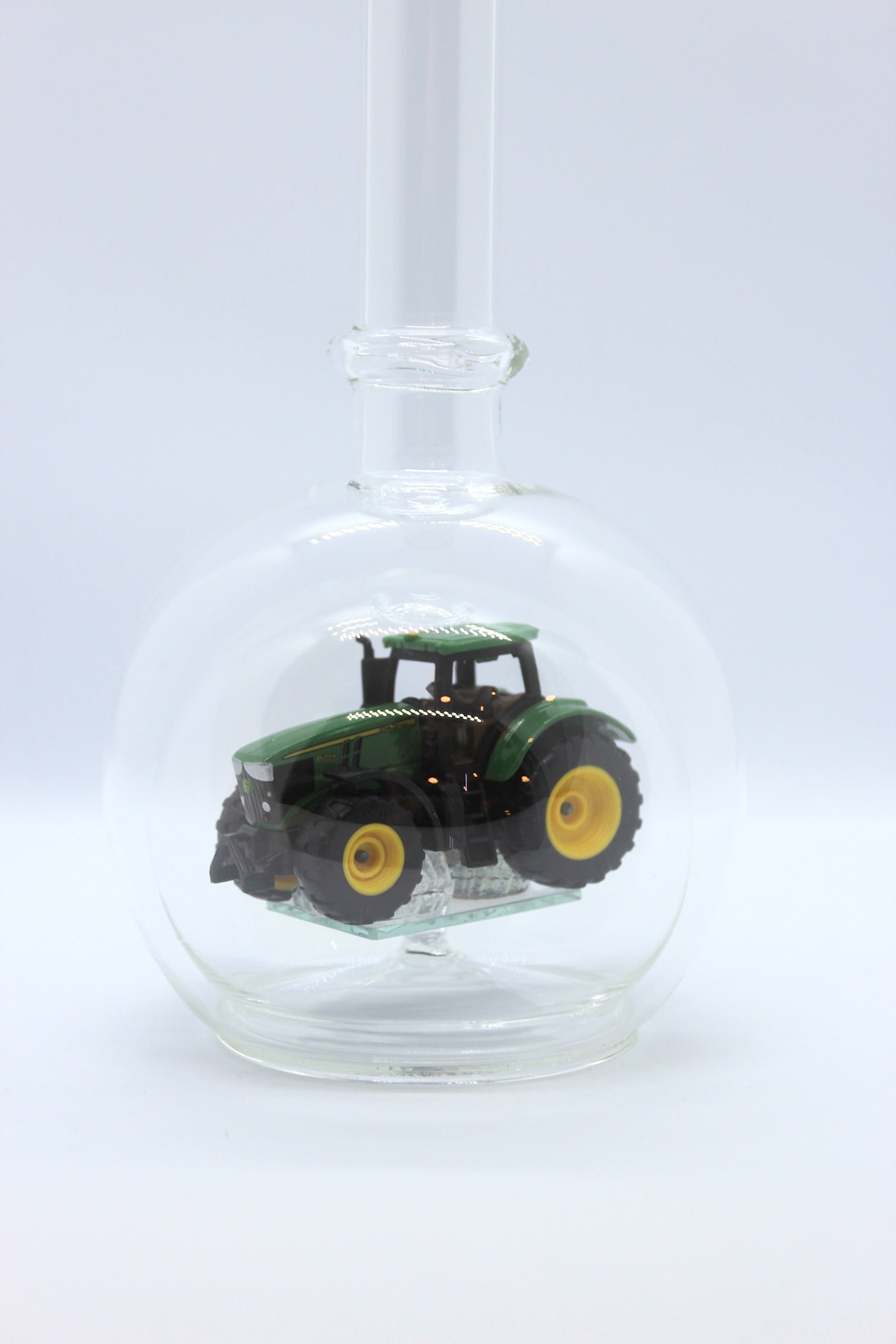Eine leere bauchige Flasche aus Glas mit einem John-Deere-Traktor im Inneren.