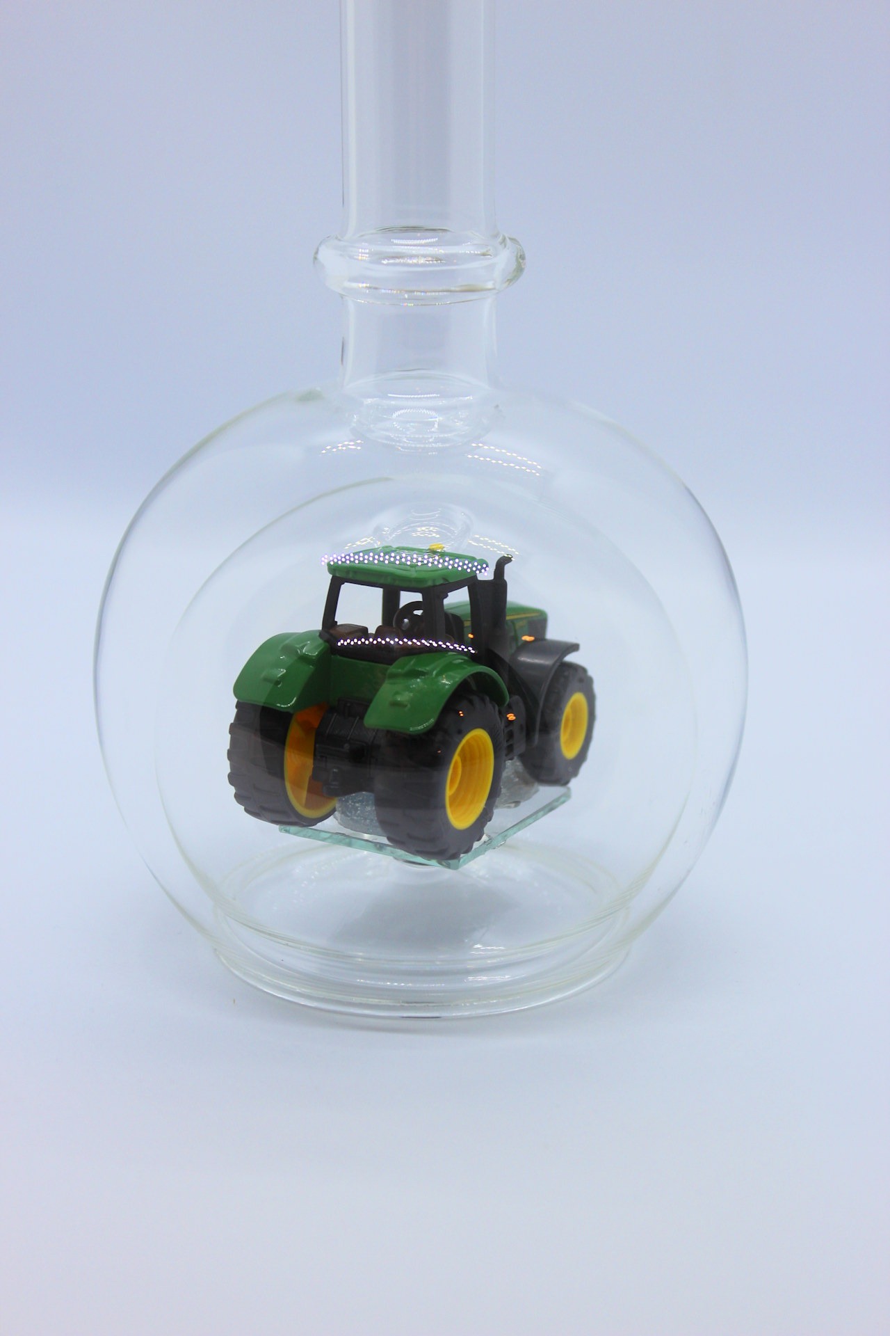 Eine leere bauchige Flasche aus Glas mit einem John-Deere-Traktor im Inneren.