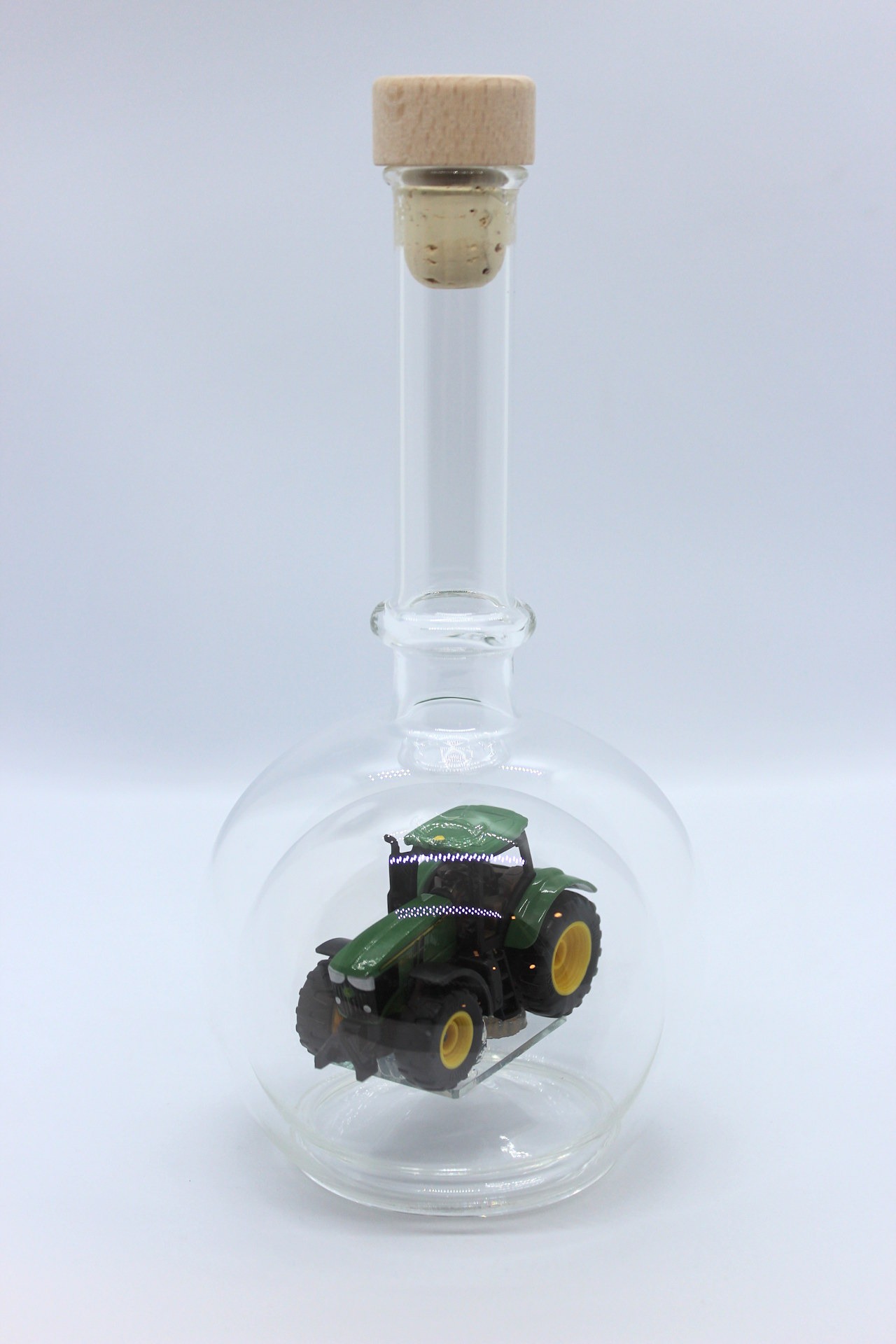 Eine leere bauchige Flasche aus Glas mit einem John-Deere-Traktor im Inneren.