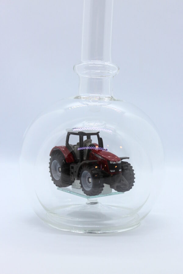 Eine leere bauchige Flasche aus Glas mit einem Massey-Ferguson-Traktor im Inneren.