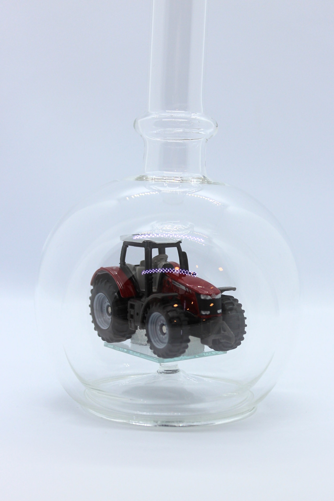 Eine leere bauchige Flasche aus Glas mit einem Massey-Ferguson-Traktor im Inneren.