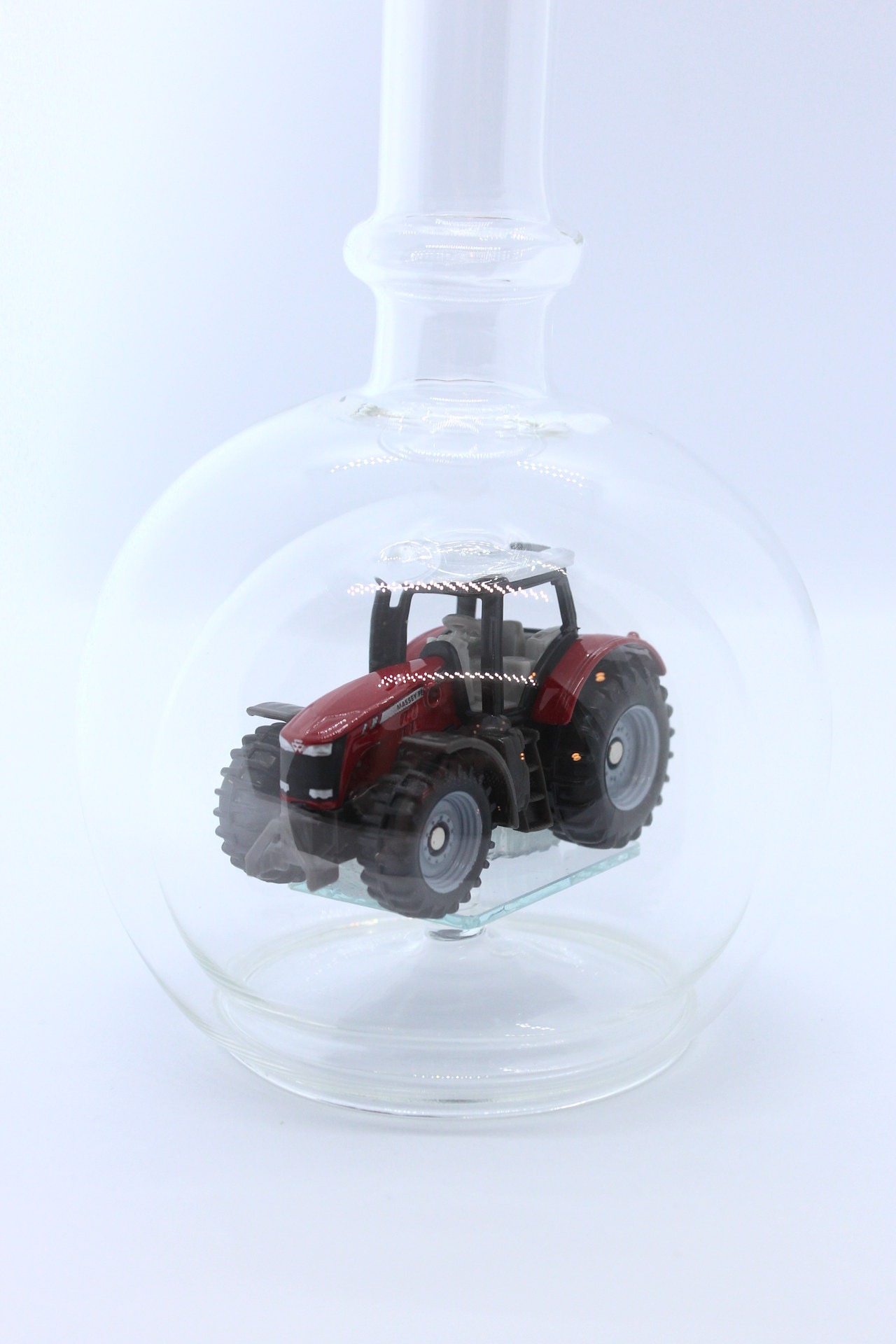 Eine leere bauchige Flasche aus Glas mit einem Massey-Ferguson-Traktor im Inneren.
