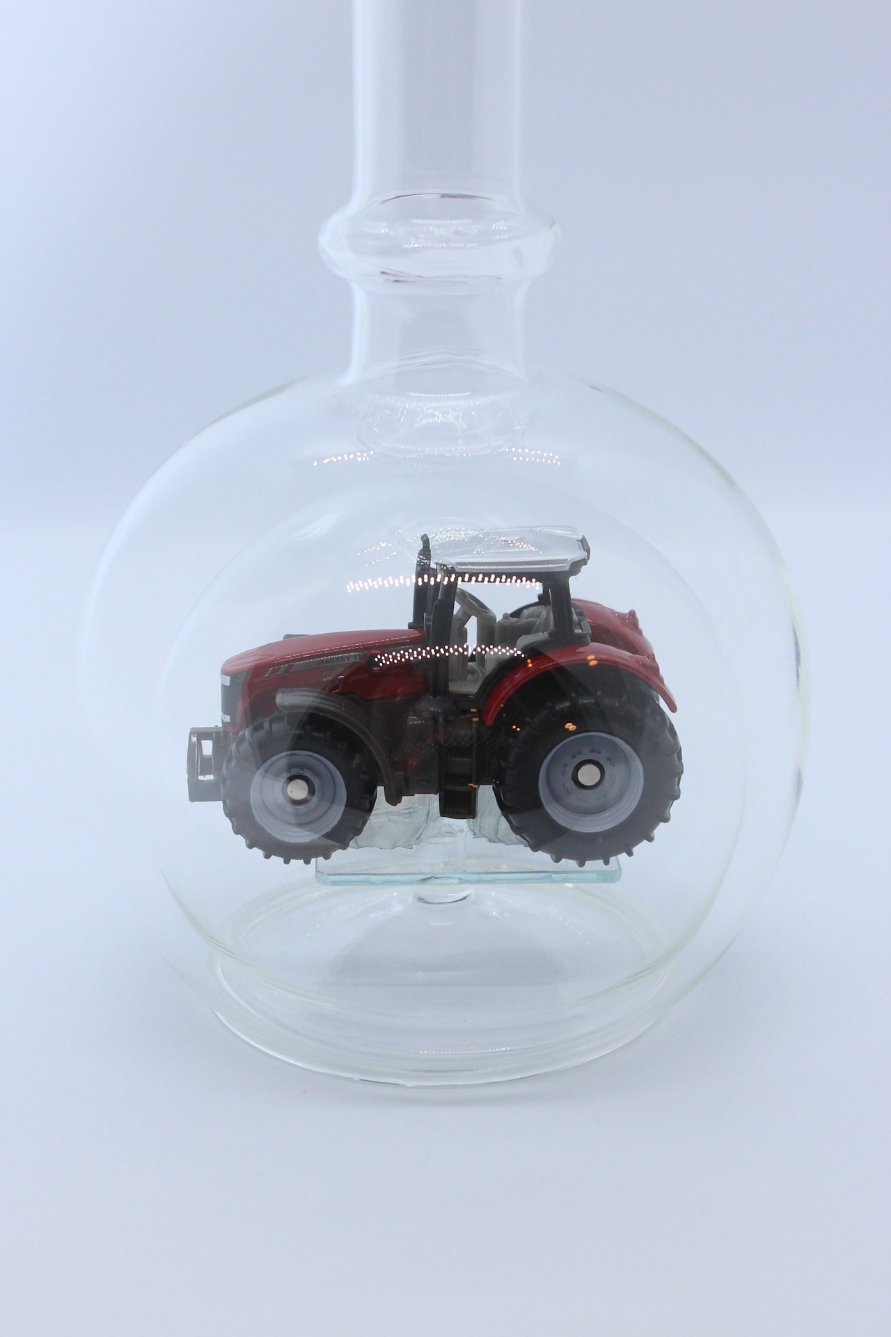 Eine leere bauchige Flasche aus Glas mit einem Massey-Ferguson-Traktor im Inneren.