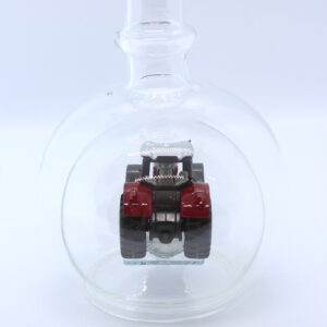 Eine leere bauchige Flasche aus Glas mit einem Massey-Ferguson-Traktor im Inneren.